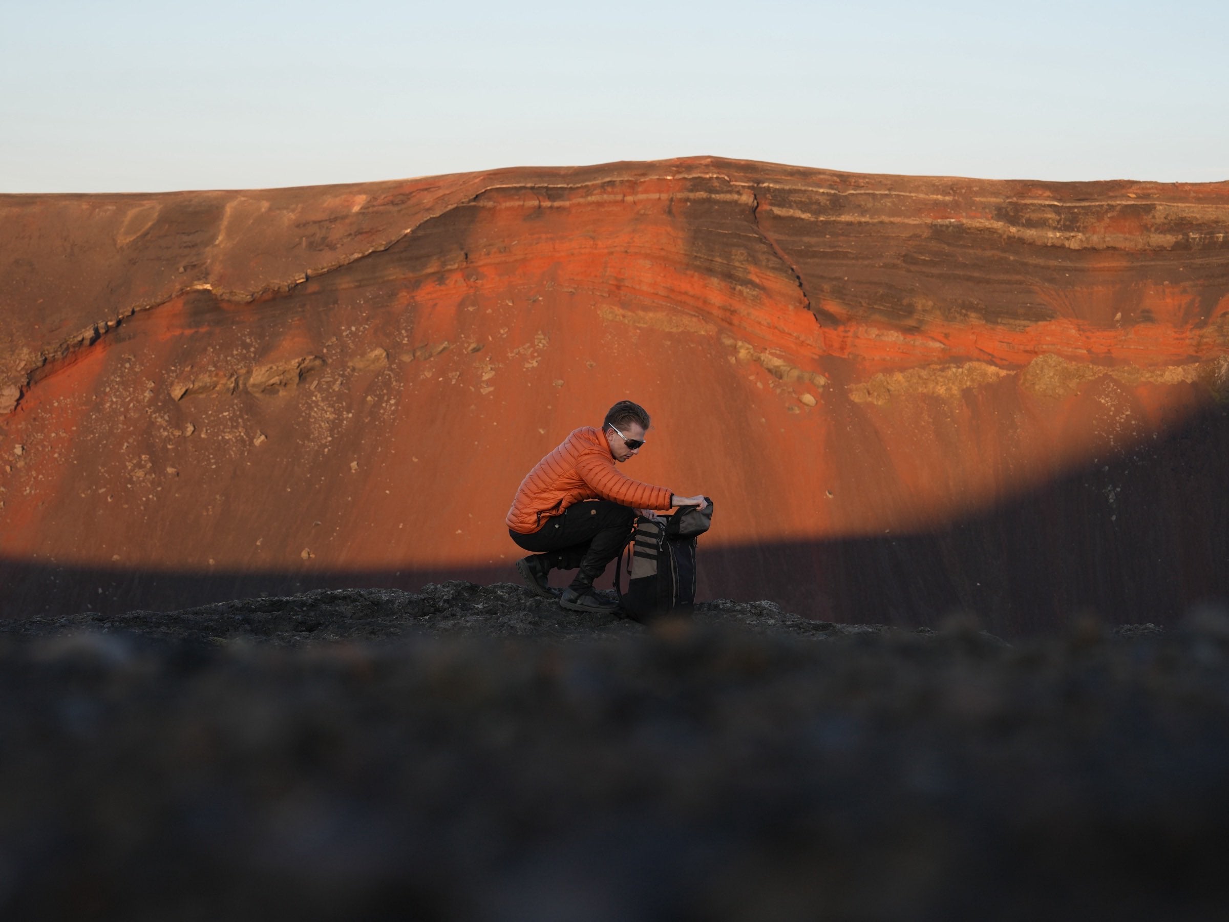 A person kneeling over an open Sentry pack on a crater rim at sunset